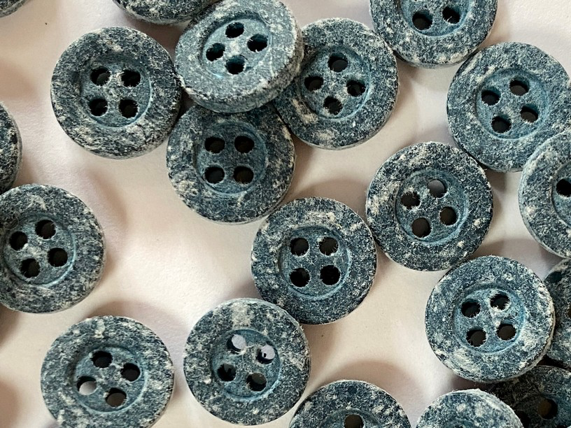 A close-up of multiple round four-hole buttons with a distressed, speckled blue-gray finish on a light neutral background.