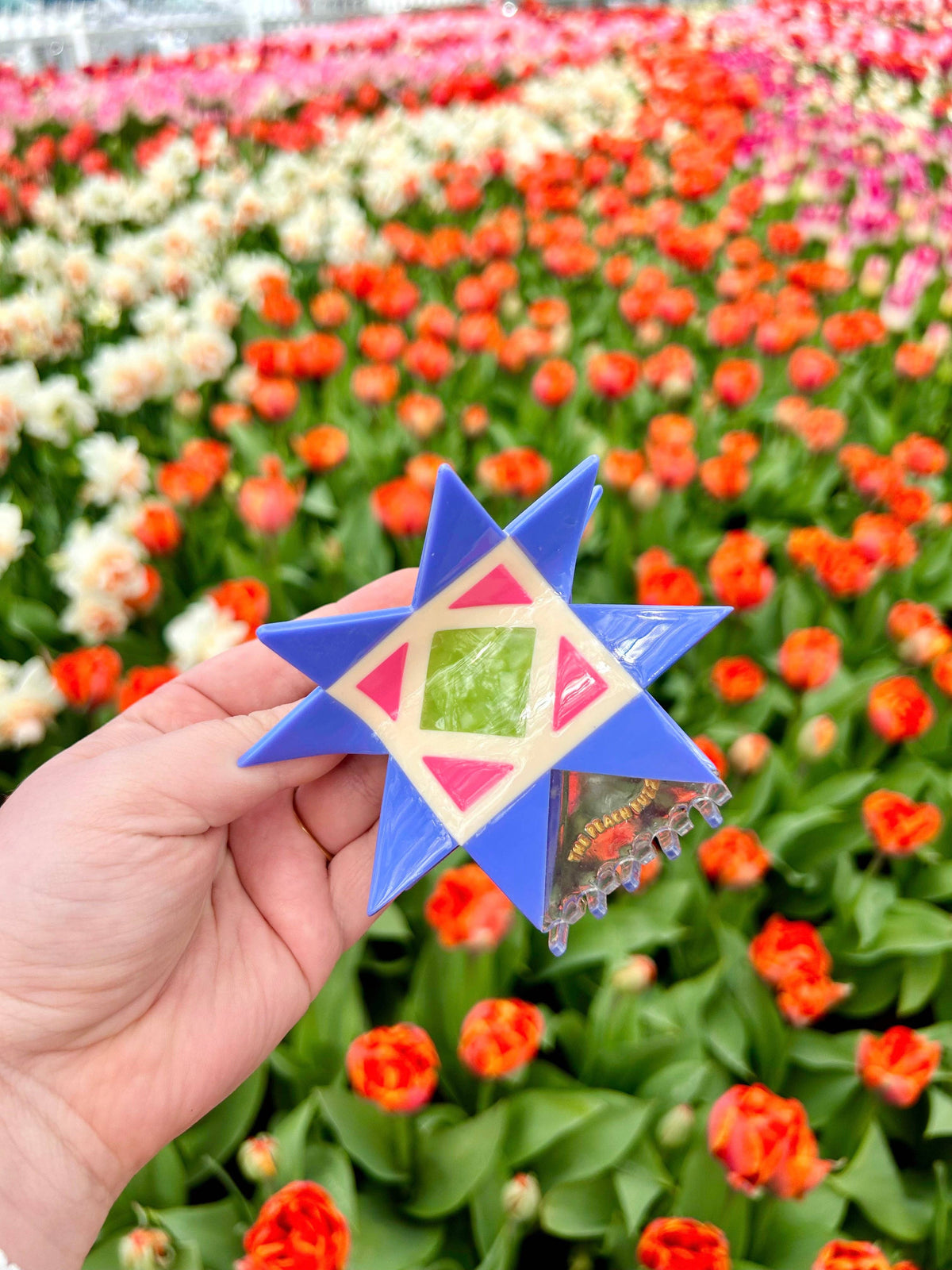 The Peach Fuzz quilt hair claw held up in a field of tulips