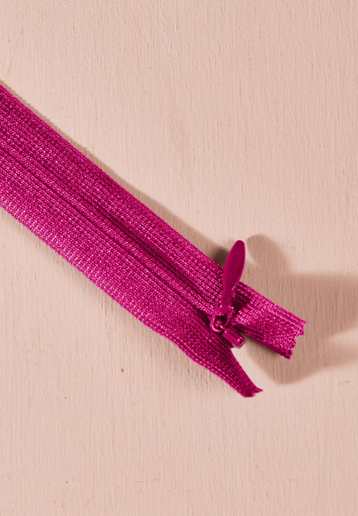 Atelier Brunette invisible zipper in bright magenta, 40 cm (16 inch), a dressmaking notion for dresses and skirts shown on a blush background