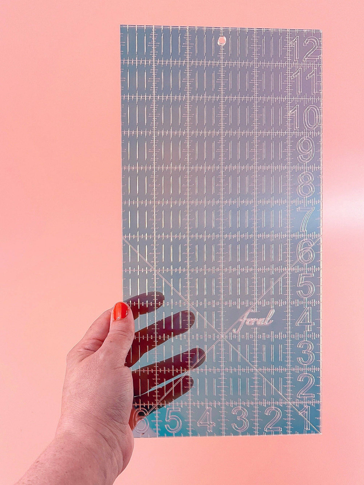 Hand holding the Feral Notions 6 x 12 inch quilting ruler in iridescent teal acrylic