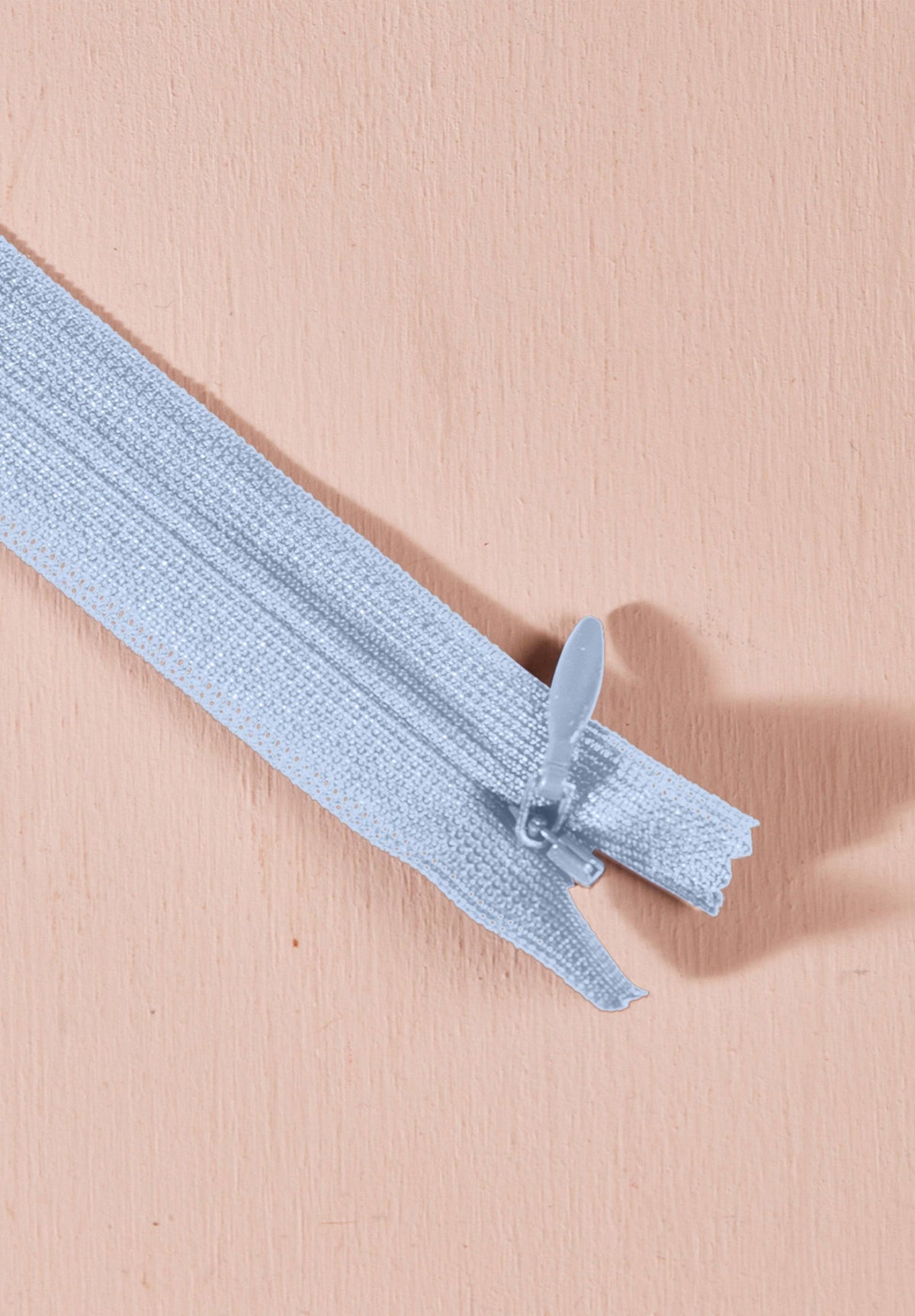 Atelier Brunette invisible zipper in light blue, angled view, 40 cm (16 inch), a dressmaking notion for dresses and skirts shown on a blush background