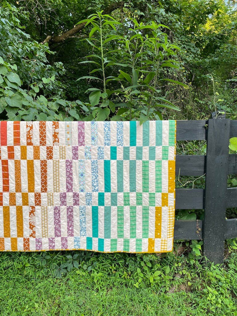 Penelope Handmade Madeline quilt pattern quilt draped on a black fence in a garden