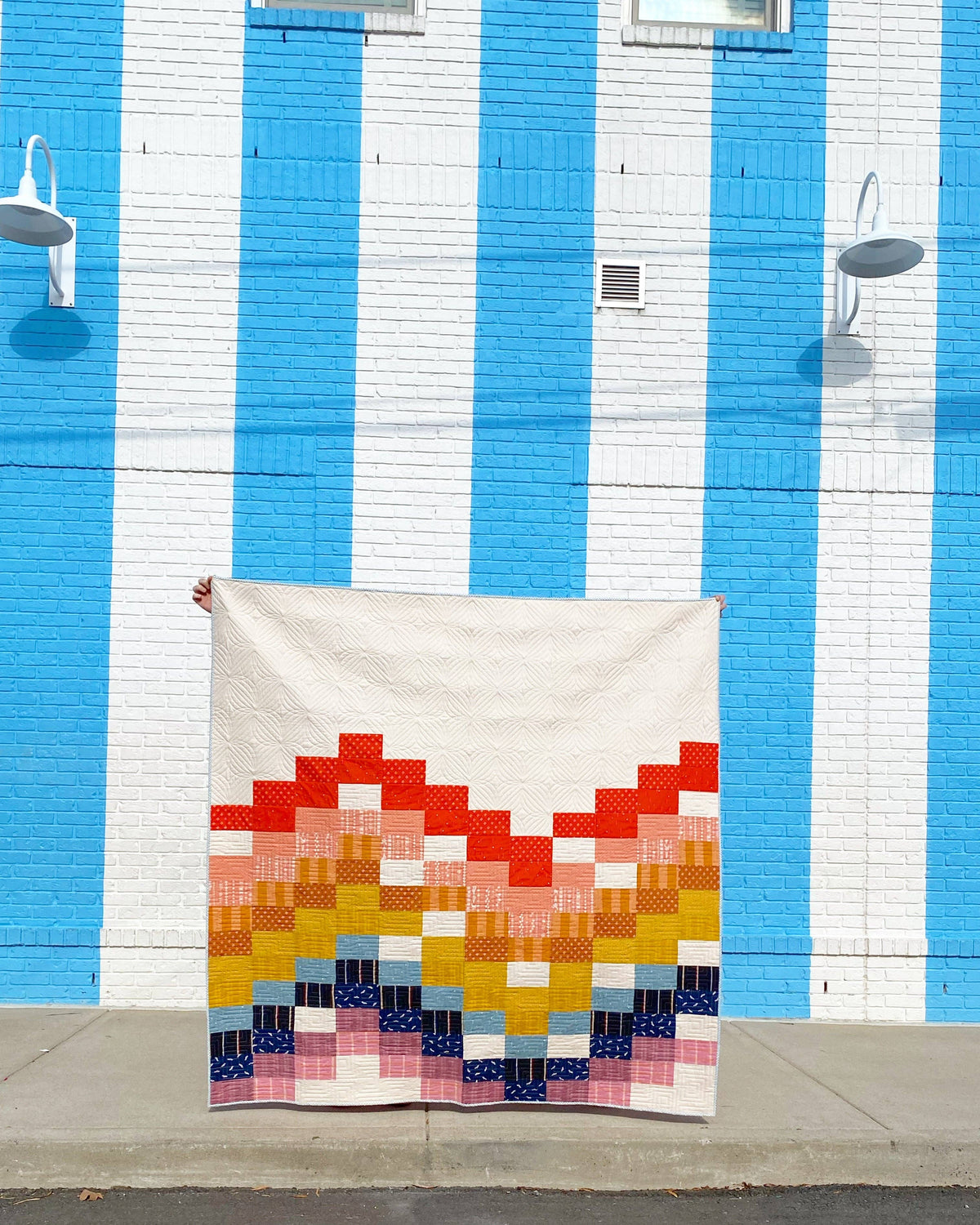 Finished Penelope Handmade Ebb and Flow quilt pattern quilt hung against a blue and white striped wall