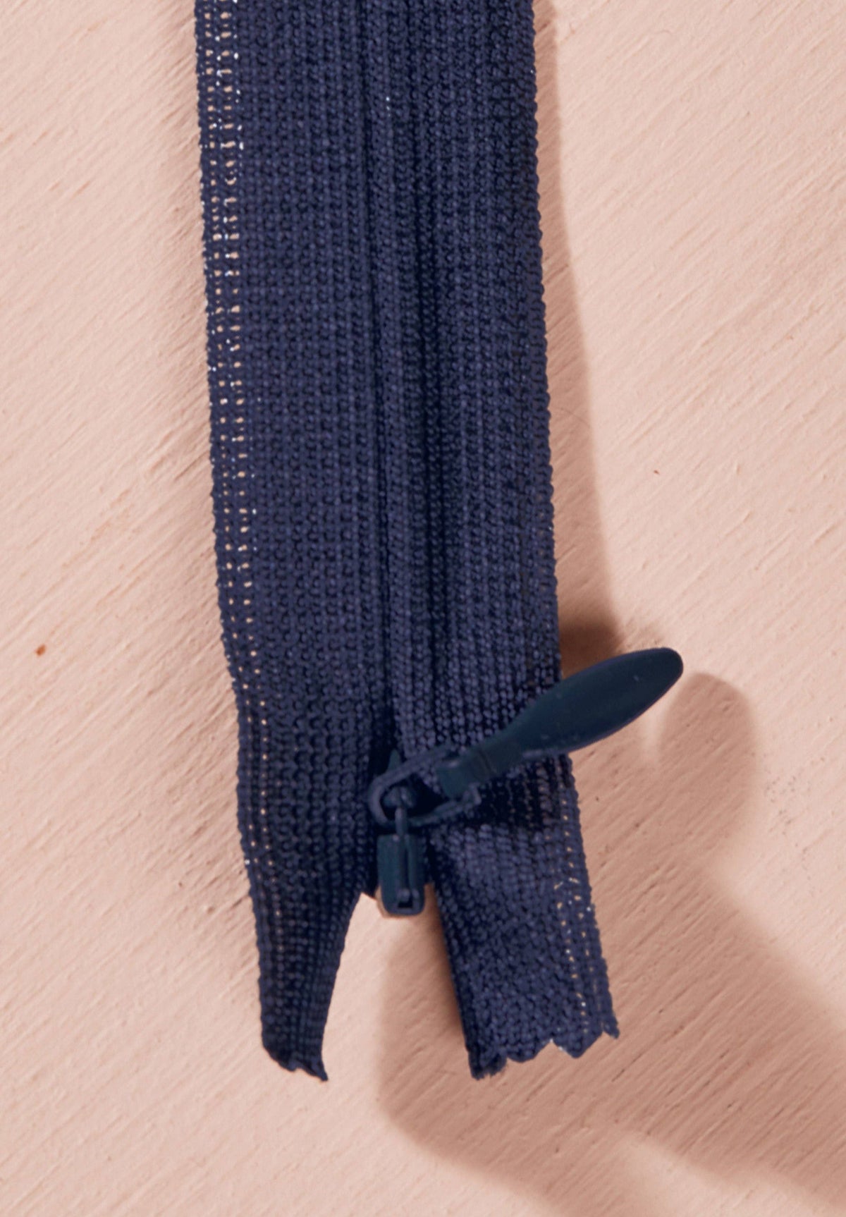 Atelier Brunette invisible zipper in navy, vertical close-up, 40 cm (16 inch), a dressmaking notion for dresses and skirts shown on a blush background