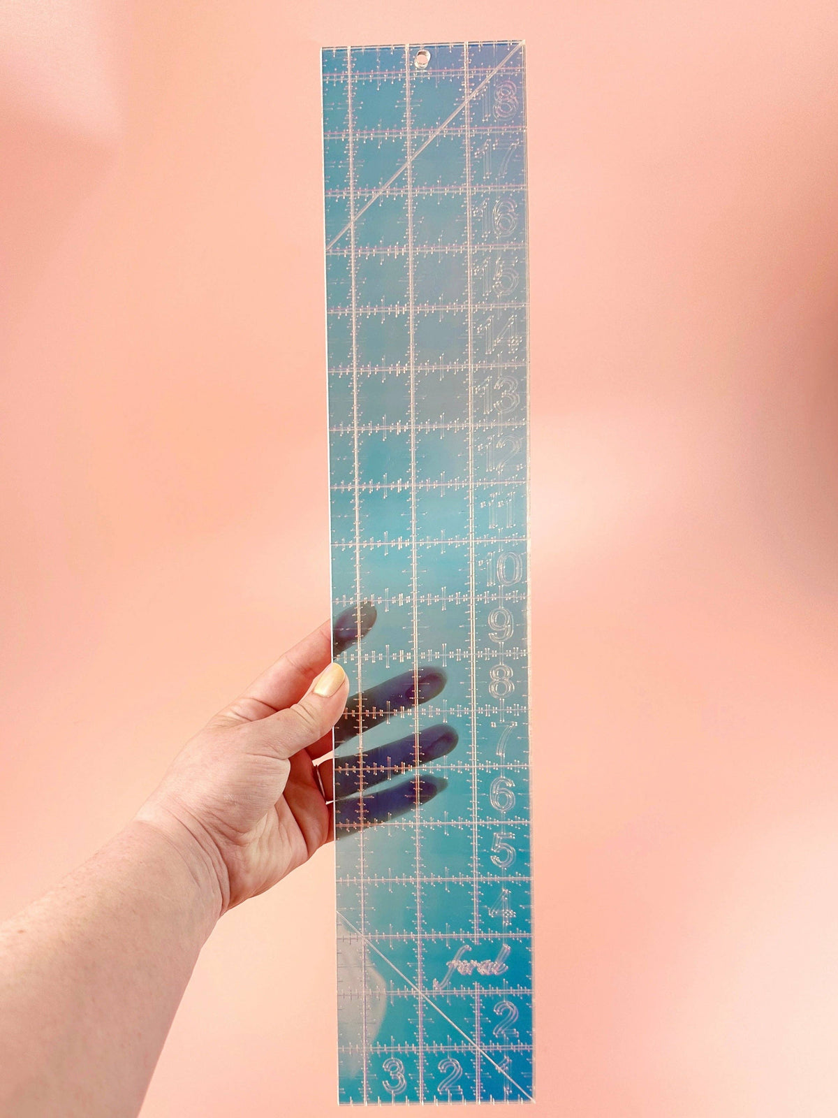 Feral Notions fat quarter quilting ruler in iridescent holographic acrylic held in hand to show the printed grid