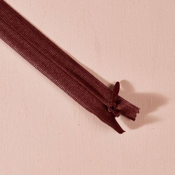 Atelier Brunette invisible zipper in dark chocolate brown, 40 cm (16 inch), a dressmaking notion for dresses and skirts shown on a blush background