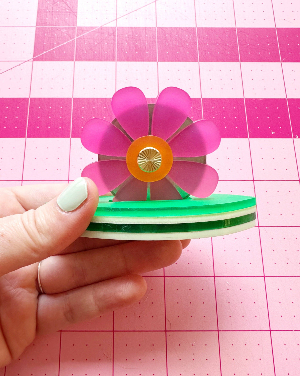 Hand holding the Feral Notions pink flower thread cutter over a cutting mat