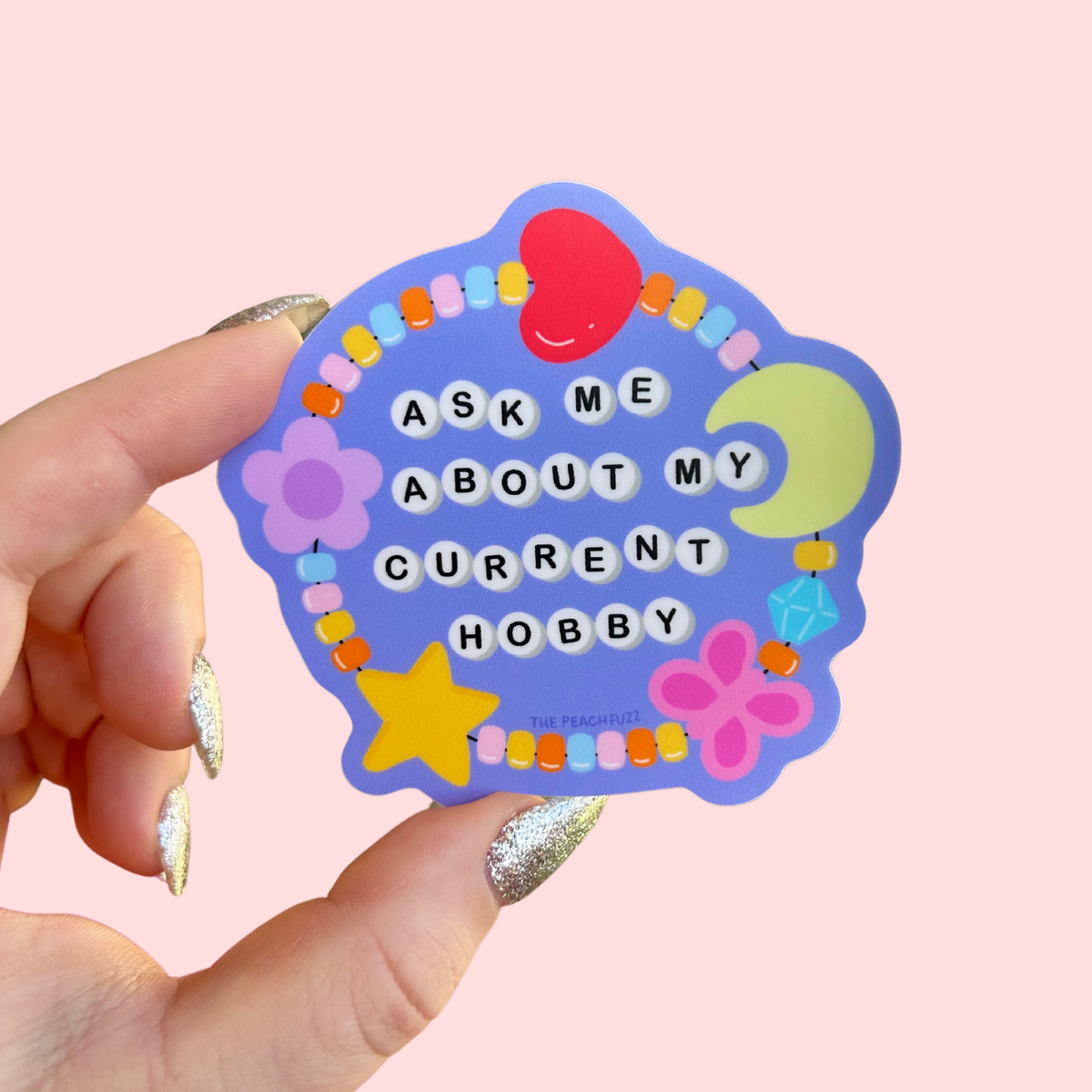 The Peach Fuzz Ask Me About My Current Hobby sticker held in hand