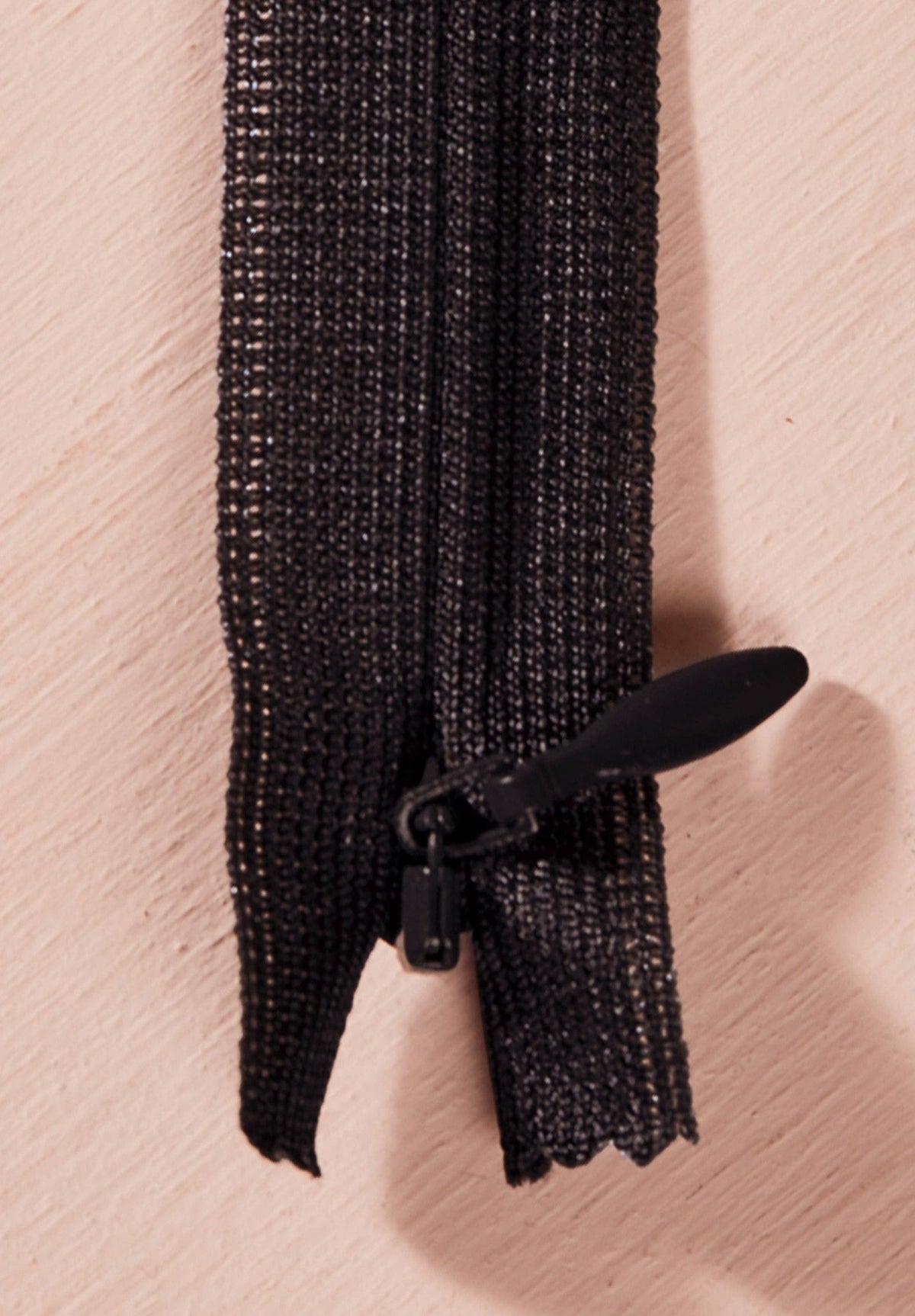 Atelier Brunette invisible zipper in black, vertical close-up, 40 cm (16 inch), a dressmaking notion for dresses and skirts shown on a blush background