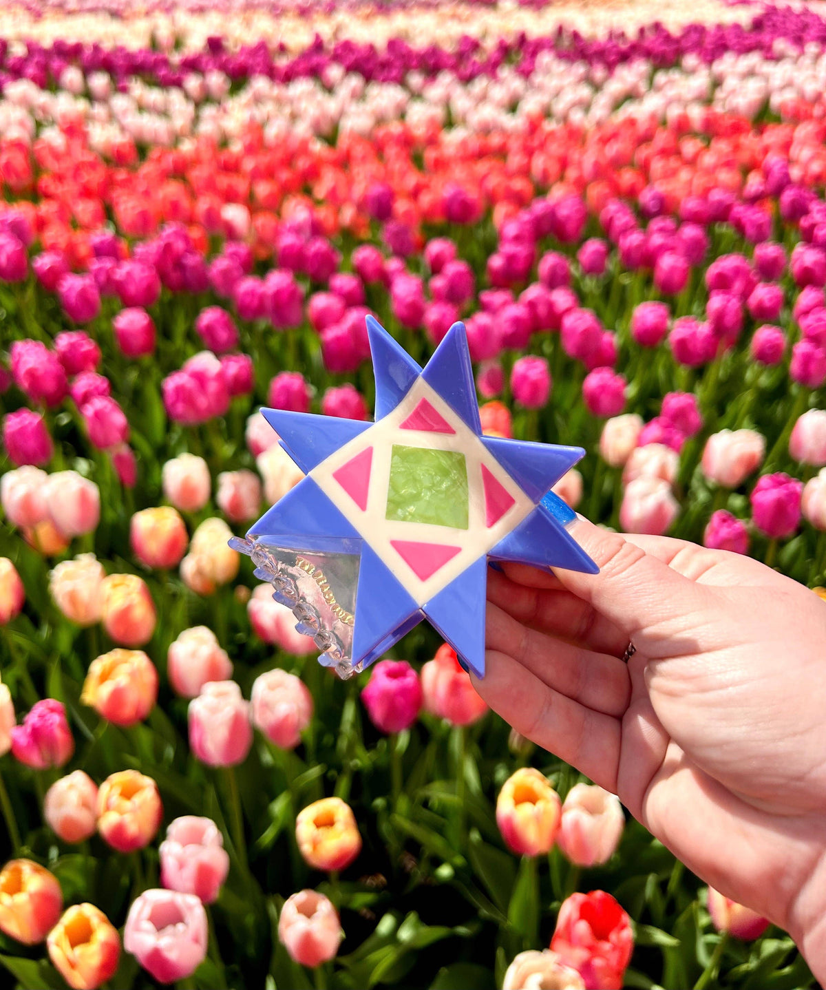 Hand holding the The Peach Fuzz quilt hair claw over red tulips