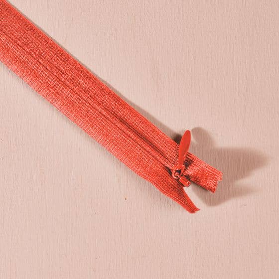 Atelier Brunette invisible zipper in coral orange, 40 cm (16 inch), a dressmaking notion for dresses and skirts shown on a blush background