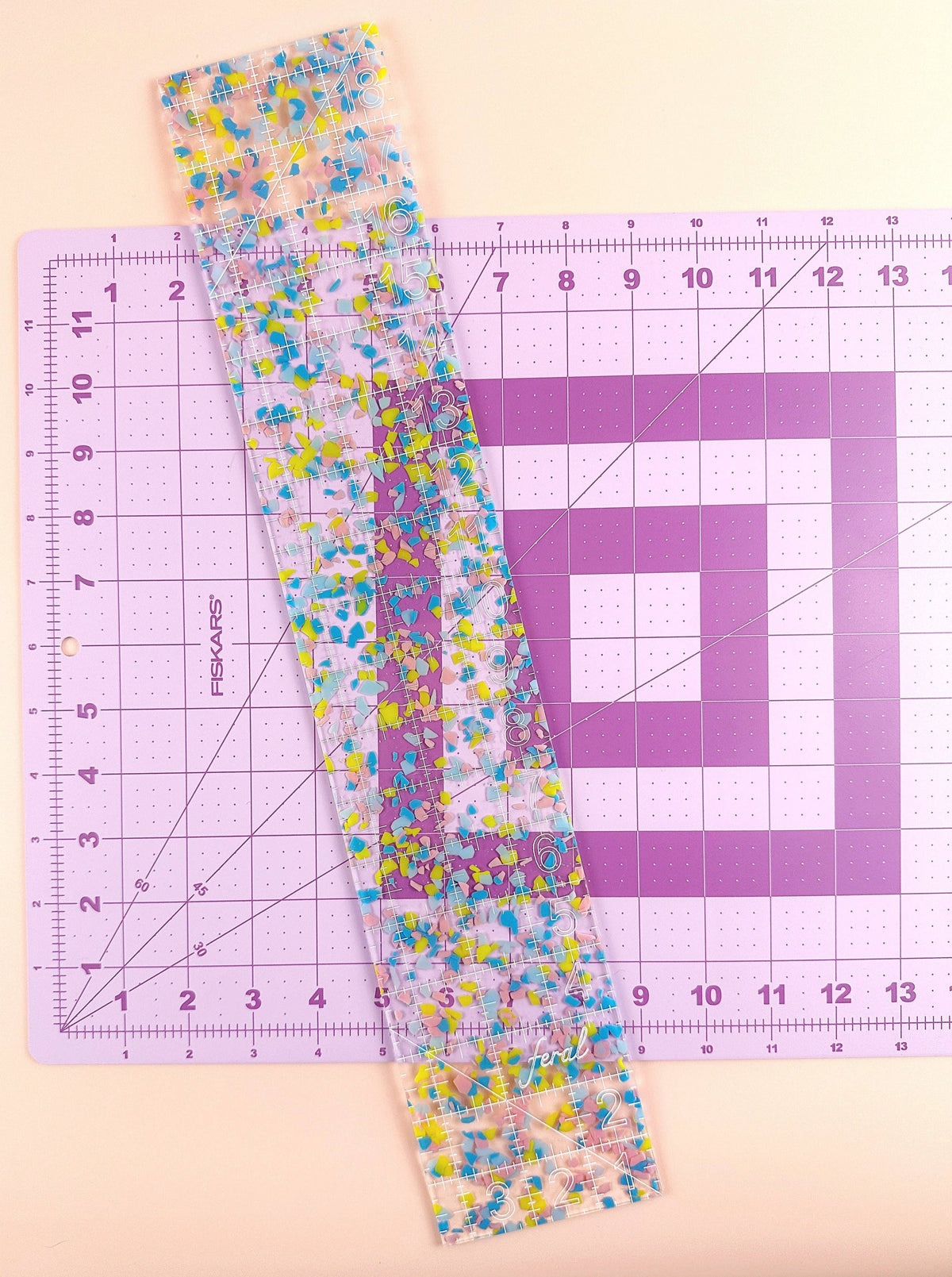 Feral Notions fat quarter quilting ruler in confetti acrylic laid on a pink cutting mat for rotary cutting fabric