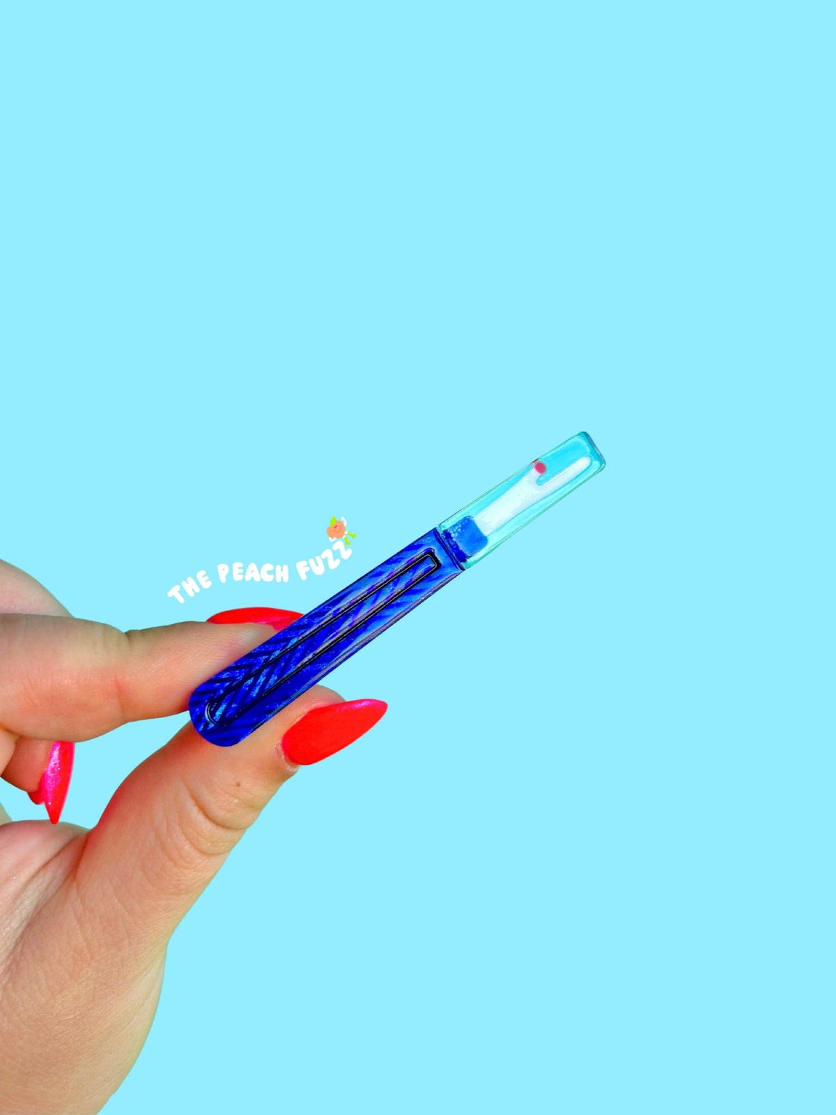 Hand holding a The Peach Fuzz needle and thread hair clip on blue