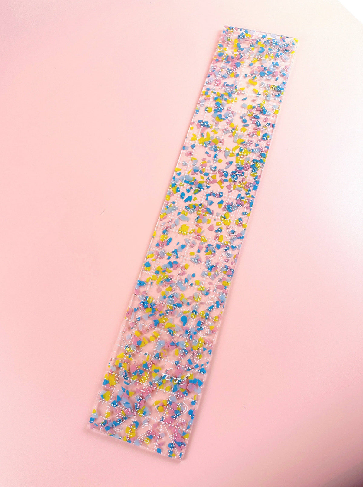 Feral Notions fat quarter quilting ruler in confetti acrylic angled on peach, a clear patchwork ruler with grid lines