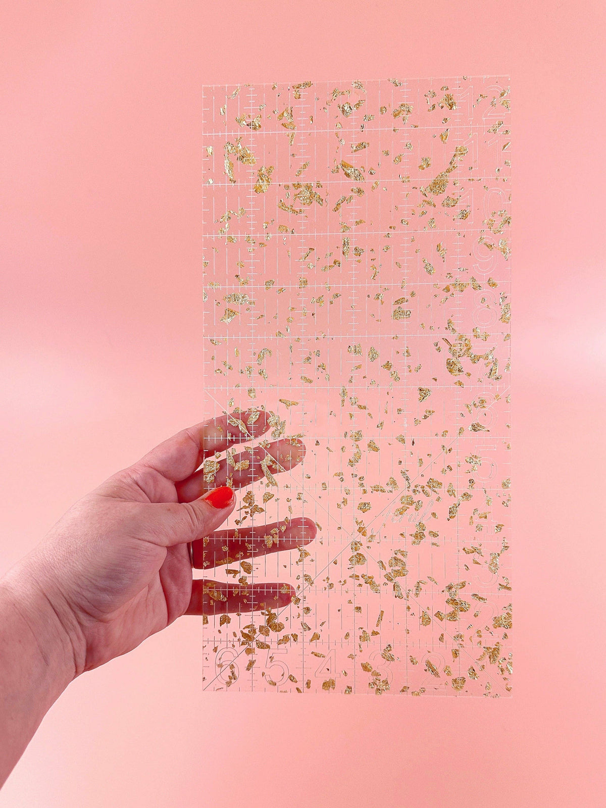 Hand holding the Feral Notions 6 x 12 inch quilting ruler in gold glitter acrylic to show the inch markings