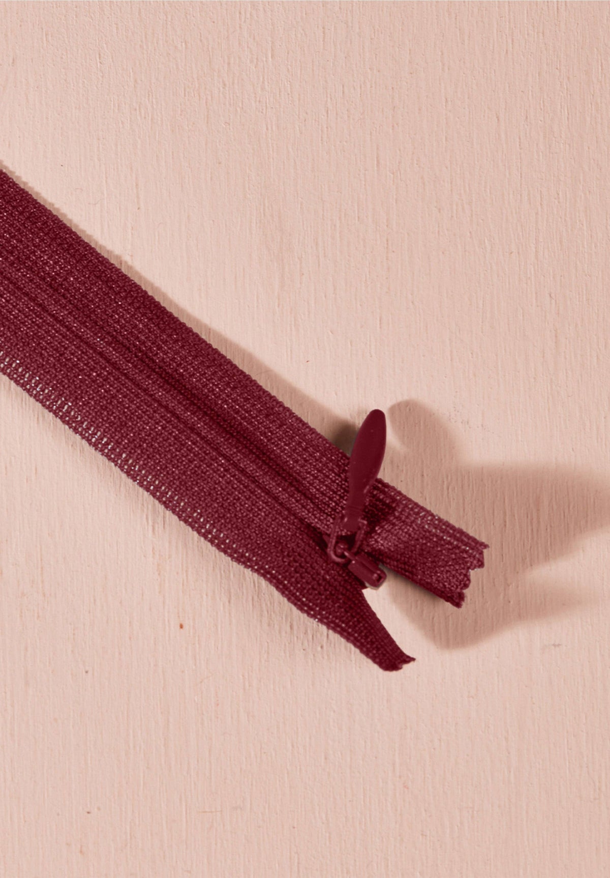 Atelier Brunette invisible zipper in burgundy, 40 cm (16 inch), a dressmaking notion for dresses and skirts shown on a blush background