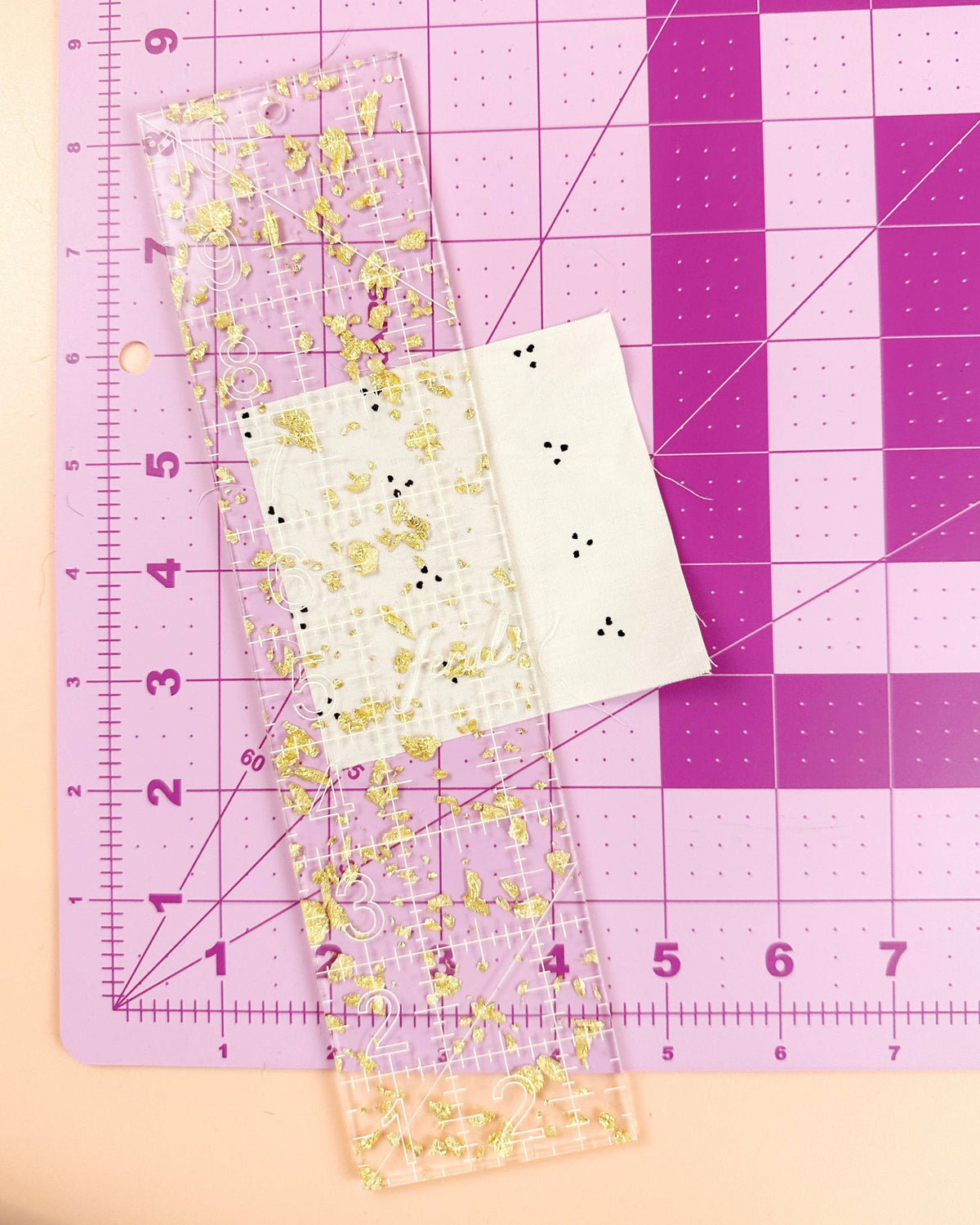 Feral Notions 2.5 x 10 inch quilting ruler in gold glitter acrylic on a pink cutting mat for cutting 2.5 inch strips