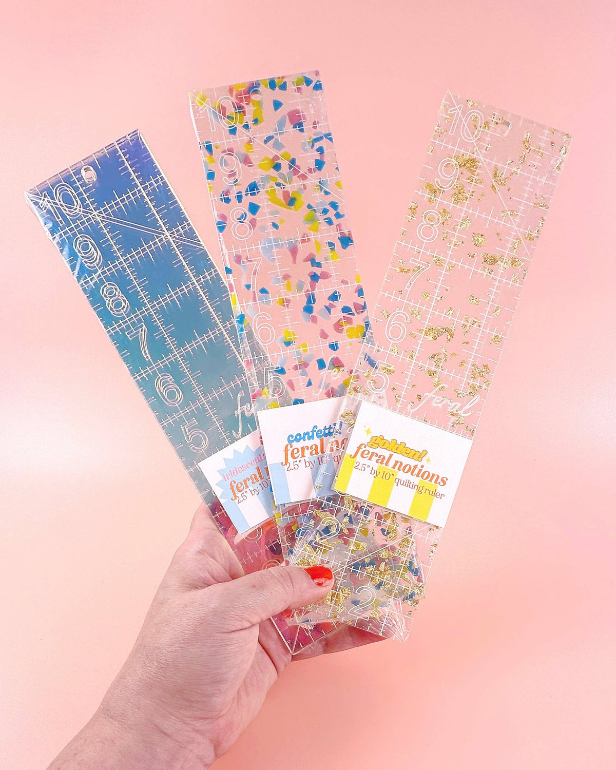 Feral Notions 2.5 x 10 inch quilting ruler set in iridescent, confetti and gold glitter acrylic fanned out in hand