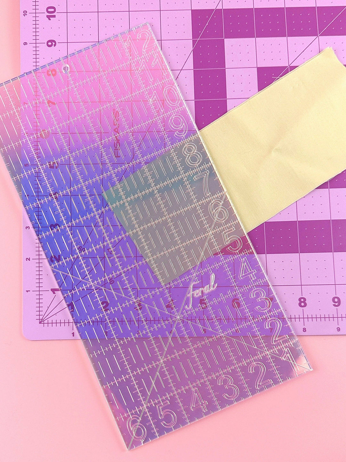 Feral Notions 6 x 12 inch quilting ruler in iridescent acrylic overlapping a gold glitter ruler on a cutting mat