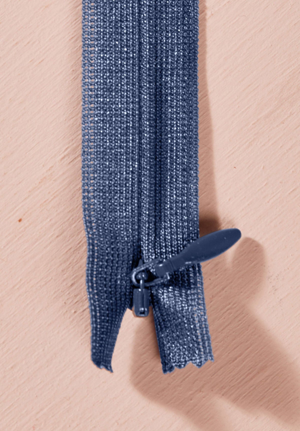 Atelier Brunette invisible zipper in denim blue, vertical close-up, 40 cm (16 inch), a dressmaking notion for dresses and skirts shown on a blush background