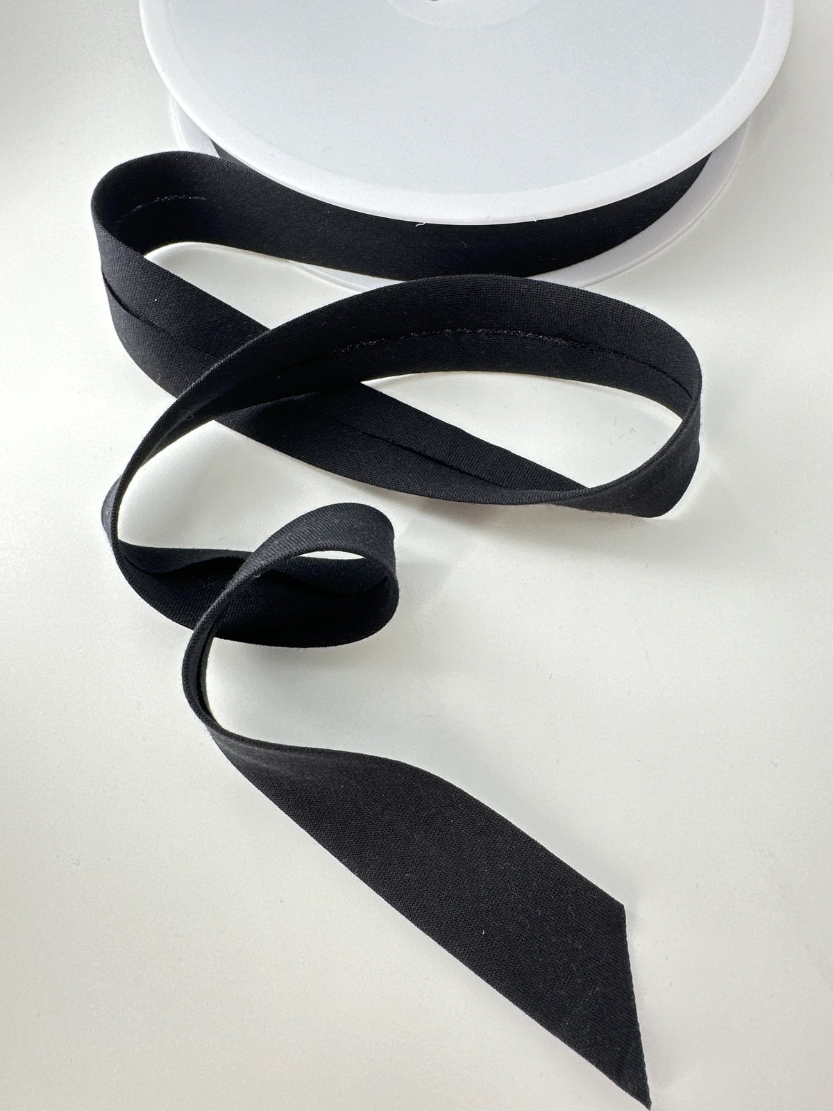 Leia crepe bias tape in black, 0.71 inch, a soft drapey bias binding coiled on white