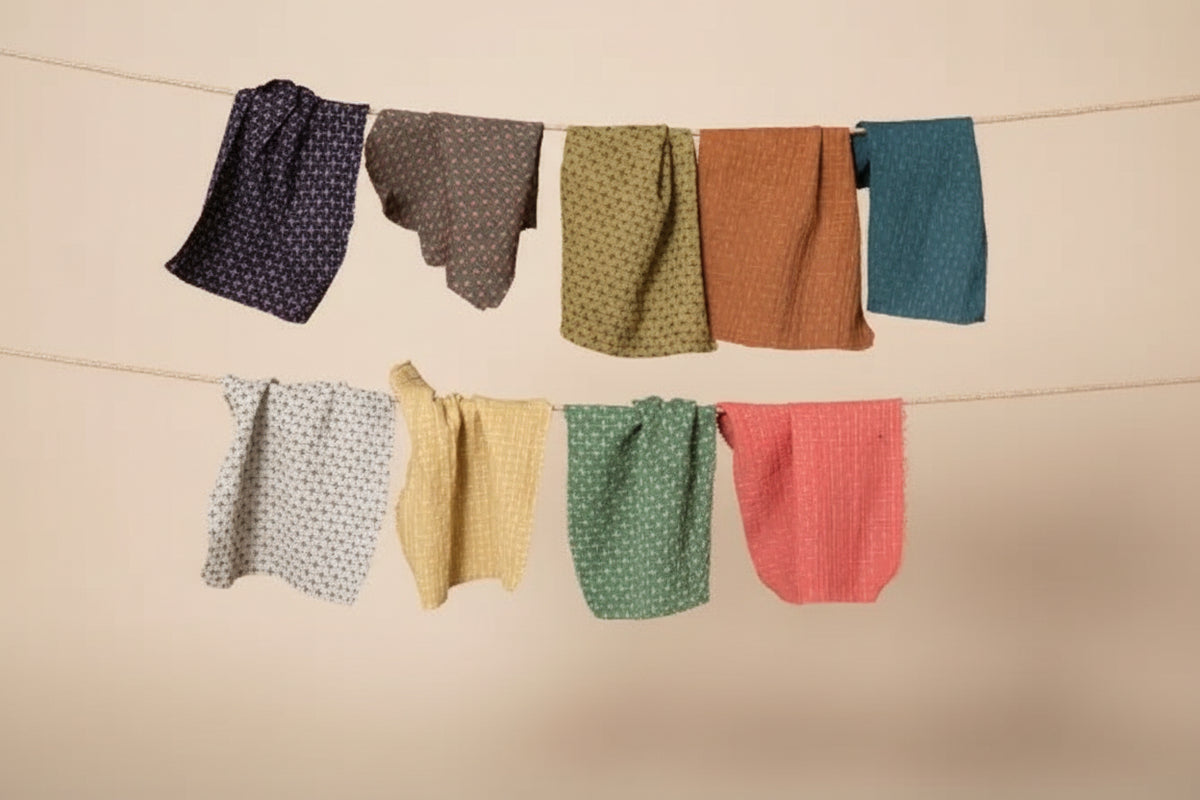 Six colorful cotton and linen fabric swatches with unique patterns are hanging from two strings like a clothesline against a dark charcoal background.