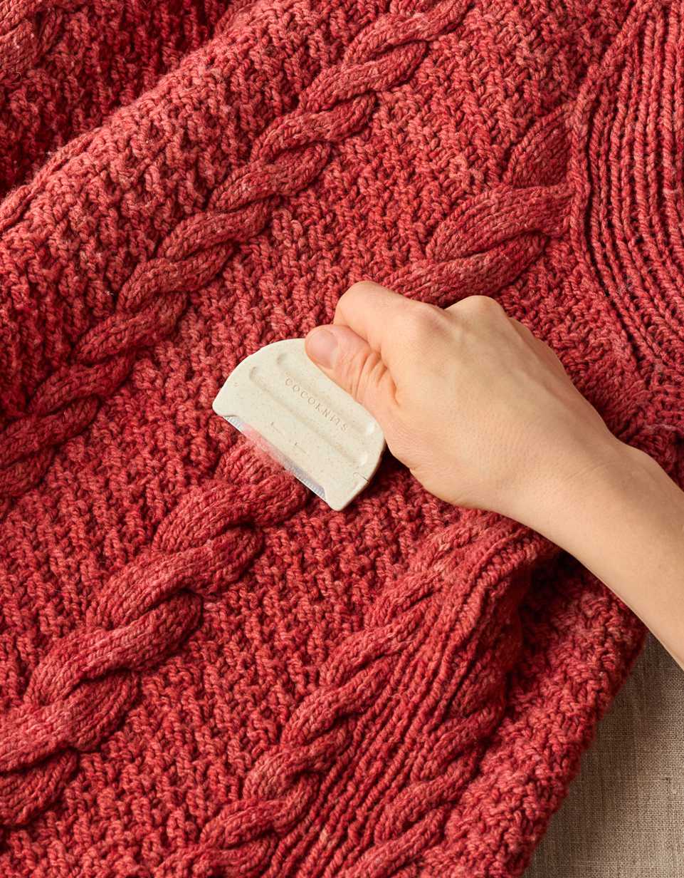 CocoKnits Fuzz Off Comb II removing pills from a red knit sweater