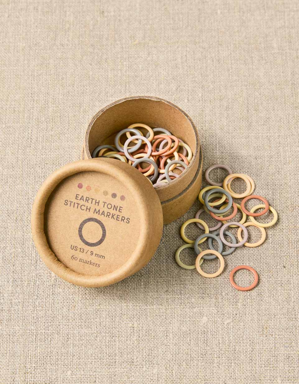 CocoKnits earth tone ring stitch markers spilling from a wooden tin