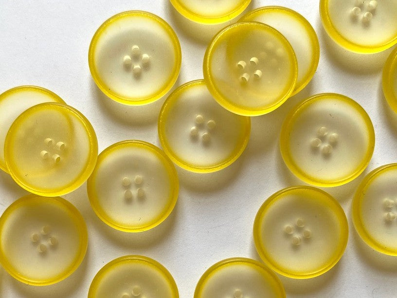 A close-up of multiple round translucent yellow buttons scattered on a plain white background.