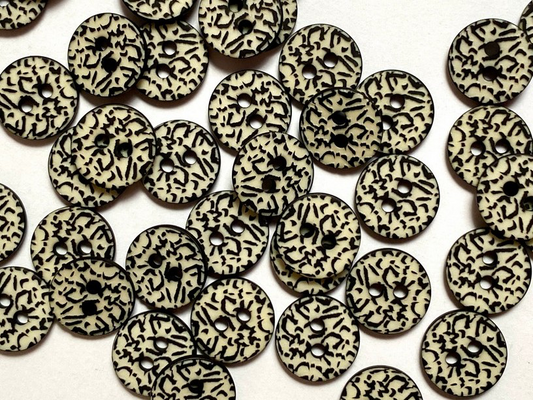 A pile of round black and cream patterned buttons with two holes, scattered on a white background.