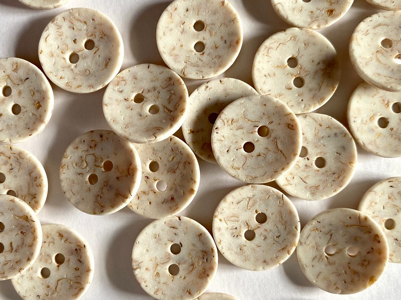 A pile of round, two-button fabric buttons with a cream-colored base and light brown marbled inclusions, arranged on a white background.