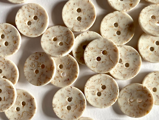 A pile of round, two-button fabric buttons with a cream-colored base and light brown marbled inclusions, arranged on a white background.