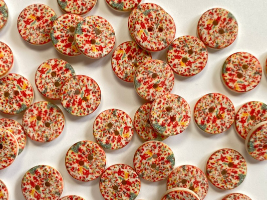 A pile of round buttons featuring red and yellow speckles on a white base with a small hole in the center, laid out on a white background.