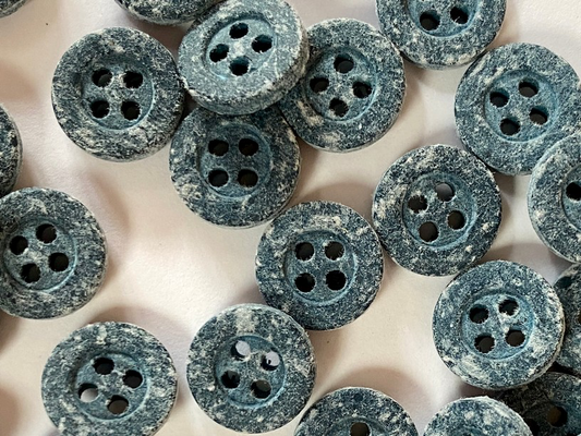 A close-up of multiple round four-hole buttons with a distressed, speckled blue-gray finish on a light neutral background.