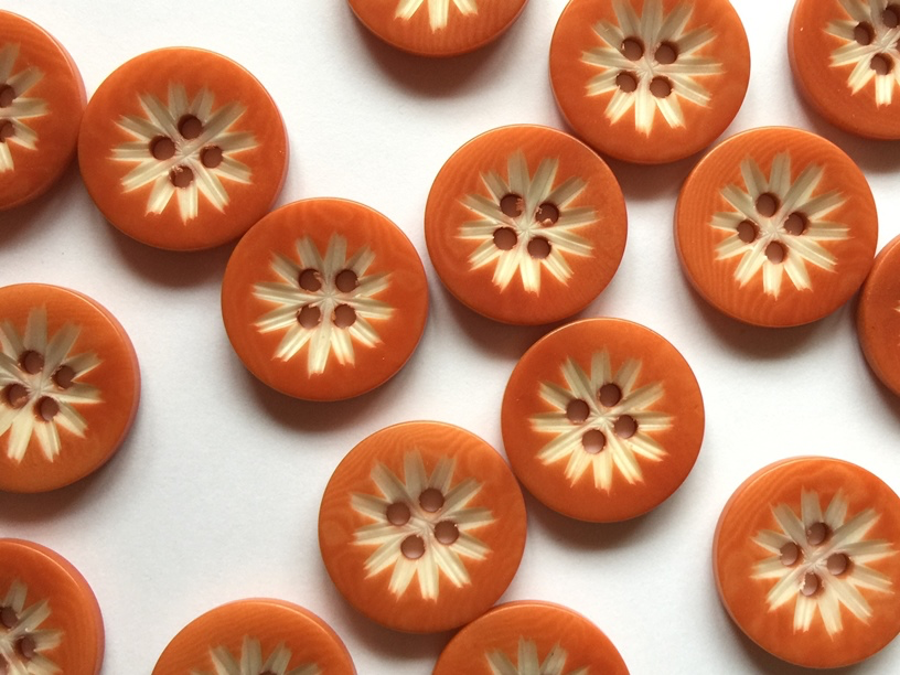 Pattern of orange buttons with floral center design on a white background