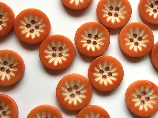 Pattern of orange buttons with floral center design on a white background
