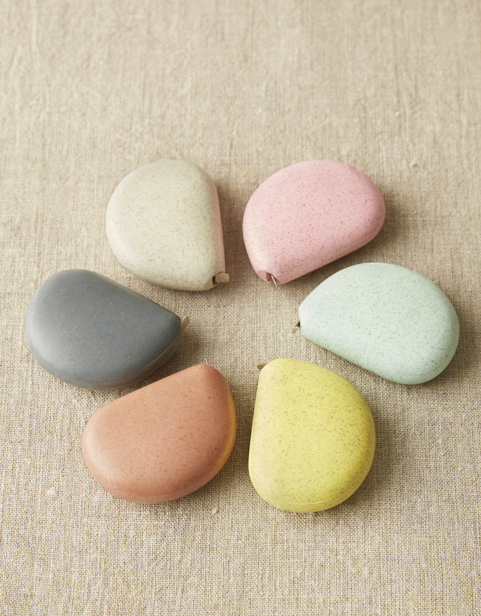 CocoKnits tape measure in Wild Rose, a pink stone shaped retractable sewing and knitting tape, in a group of six stone colors from above