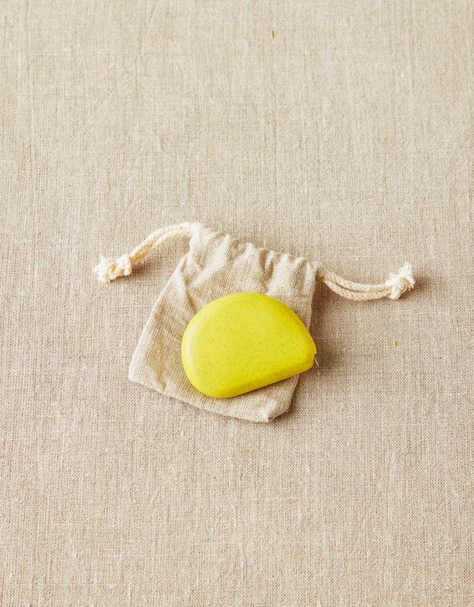 CocoKnits tape measure in Mustard Seed, a yellow stone shaped retractable sewing and knitting tape, with its cotton drawstring pouch