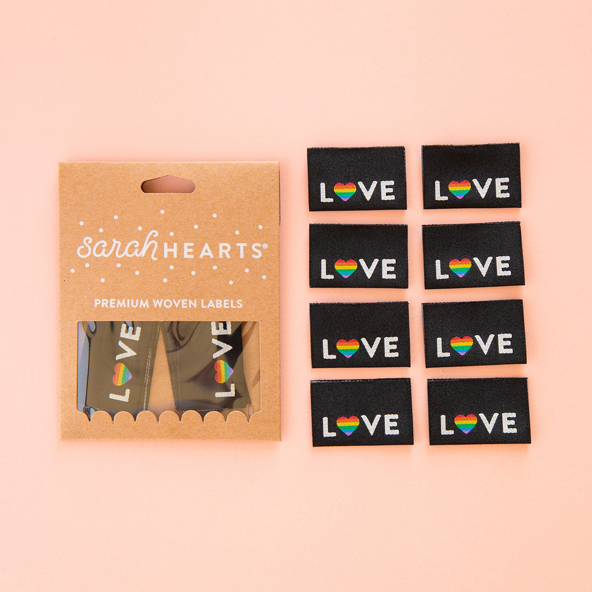 Sarah Hearts Love Pride heart woven labels in a kraft pack beside loose rainbow LOVE sew-in labels