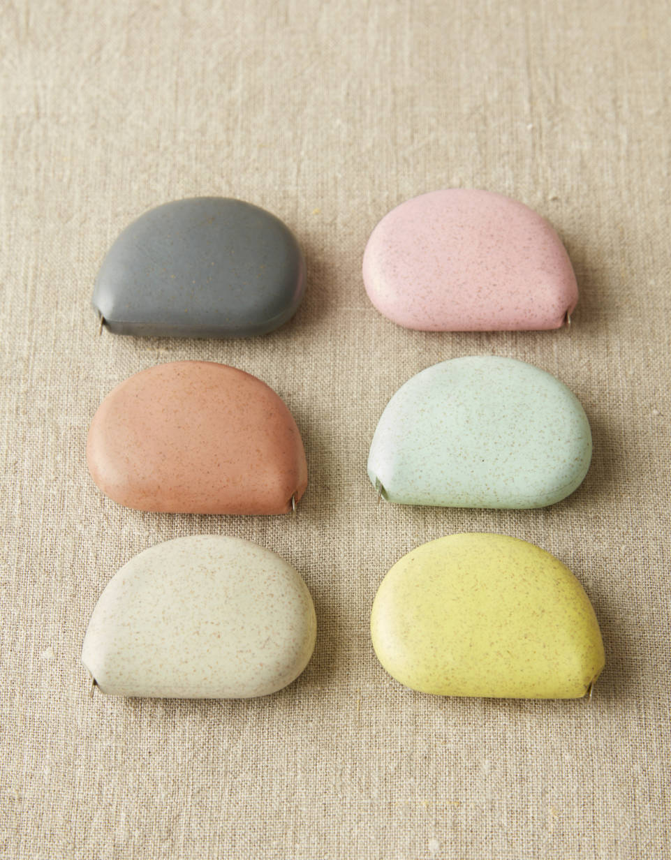 CocoKnits tape measure in Storm, a grey stone shaped retractable sewing and knitting tape, in a group of six colors, angled view