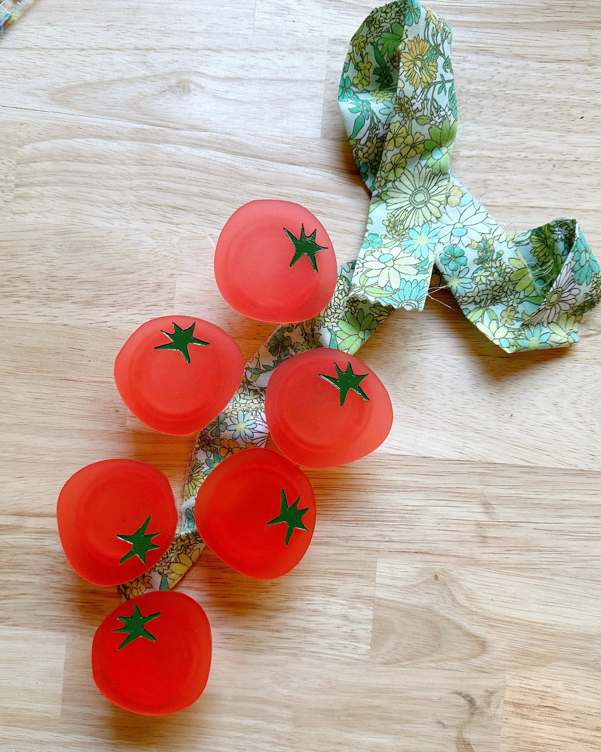 Several Feral Notions tomato pop-up ruler handles on a wood table with fabric