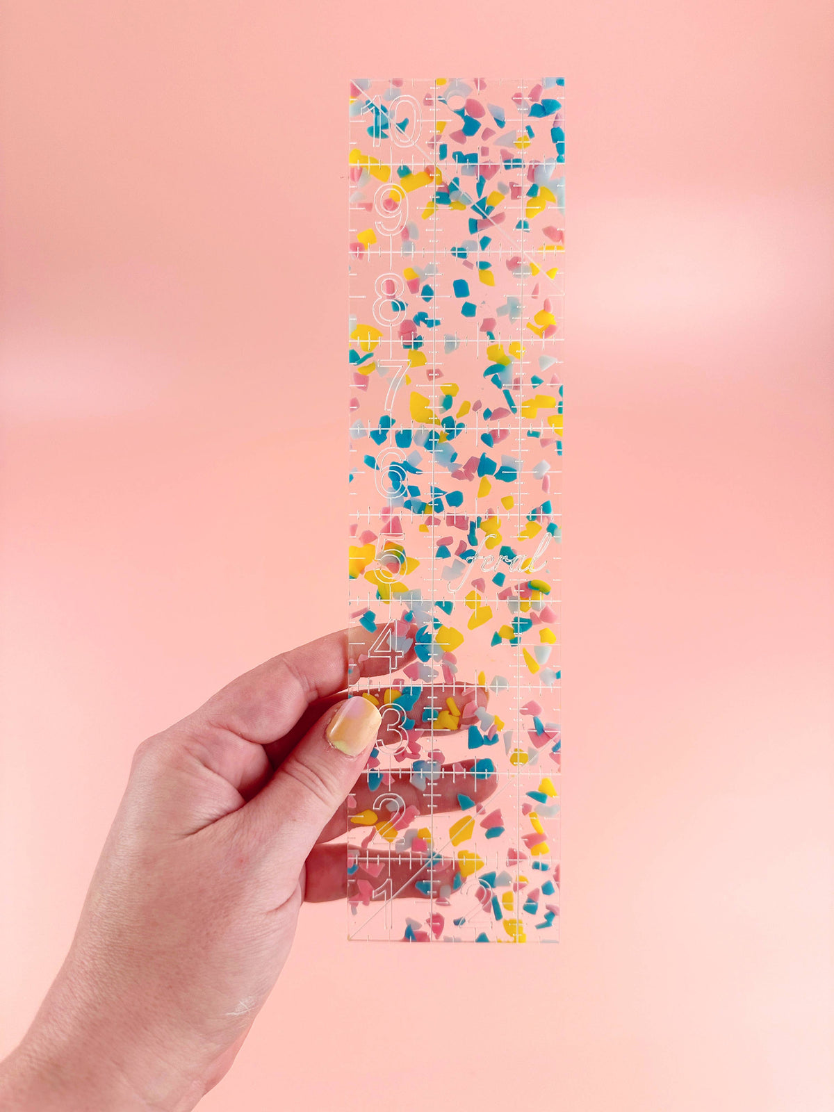 Hand holding the Feral Notions 2.5 x 10 inch quilting ruler in rainbow confetti acrylic
