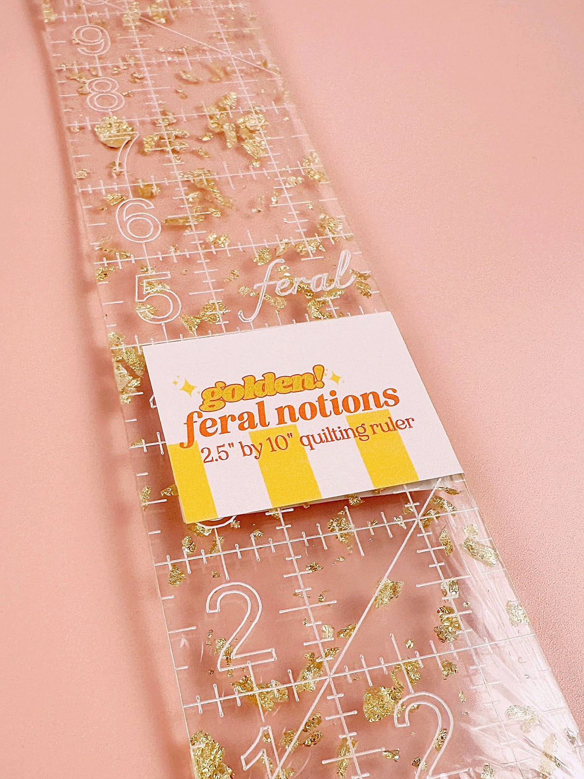 Feral Notions 2.5 x 10 inch quilting ruler in gold glitter acrylic with its label, a binding and strip ruler