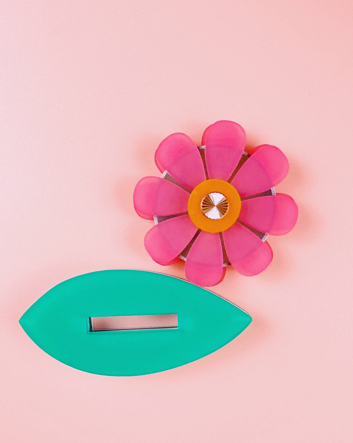 Feral Notions pink flower thread cutter with its green leaf on a peach background