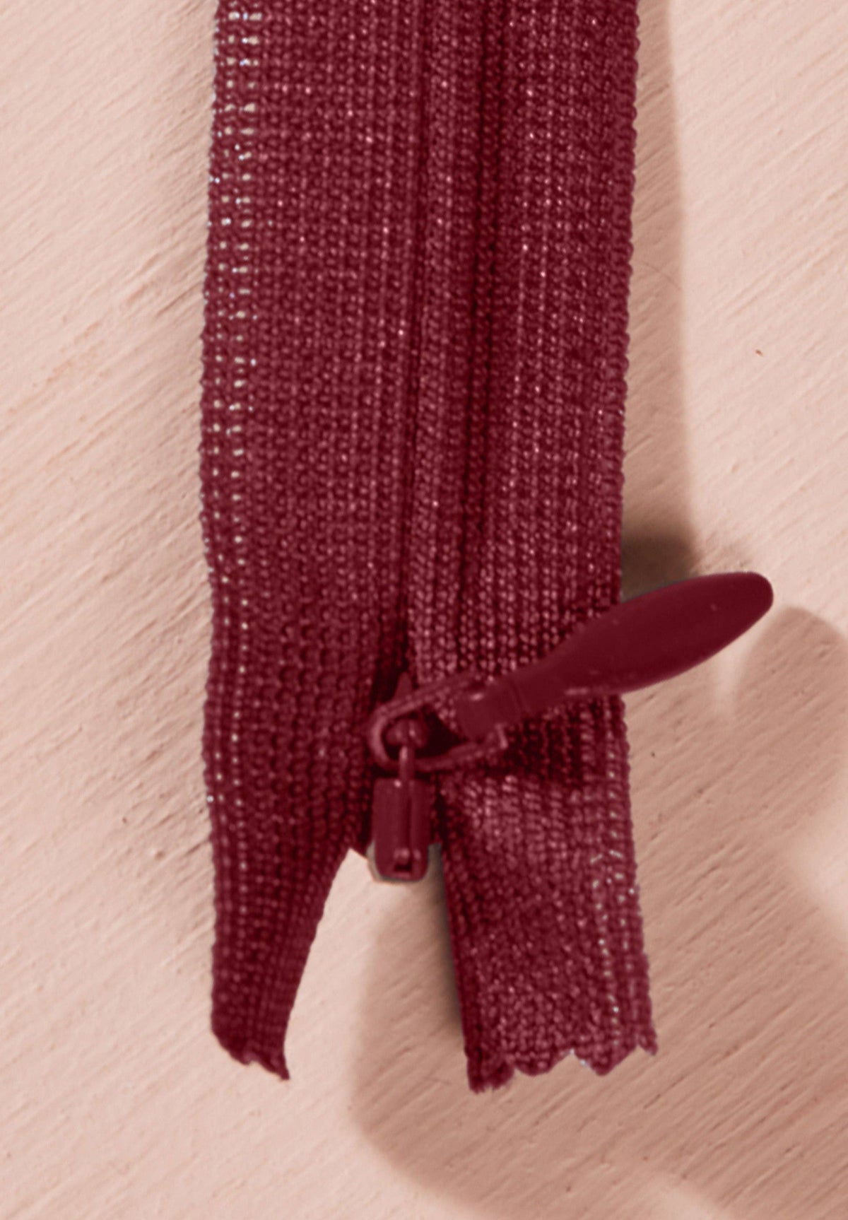 Atelier Brunette invisible zipper in deep burgundy, vertical close-up, 40 cm (16 inch), a dressmaking notion for dresses and skirts shown on a blush background