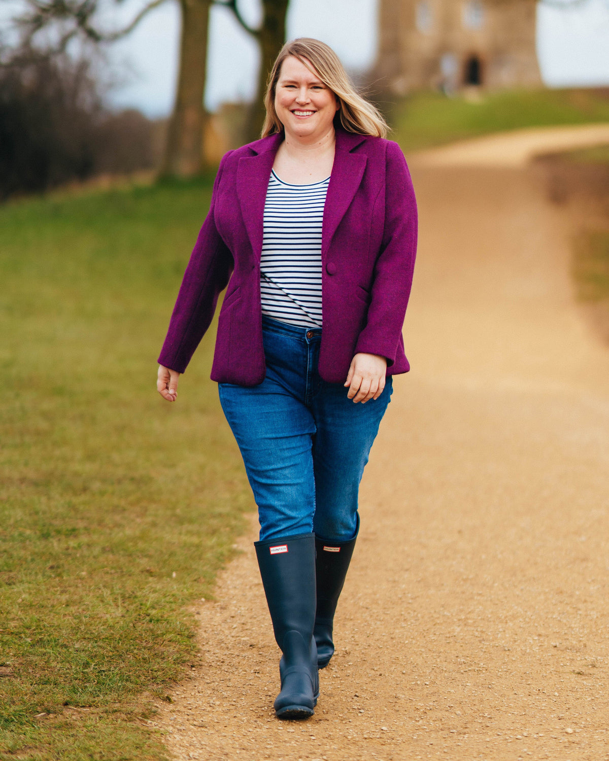 Cashmerette Auburn Blazer PDF sewing pattern, woman in a purple coat, striped shirt, and blue jeans walking on a path outdoors.. This blazer is the