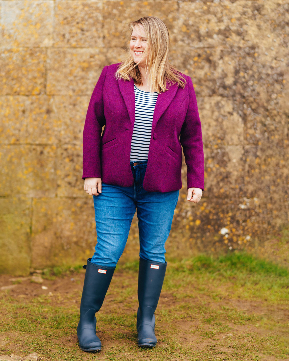 Cashmerette Auburn Blazer PDF sewing pattern, woman wearing a purple jacket, striped shirt, blue jeans, and navy boots standing in front of a stone