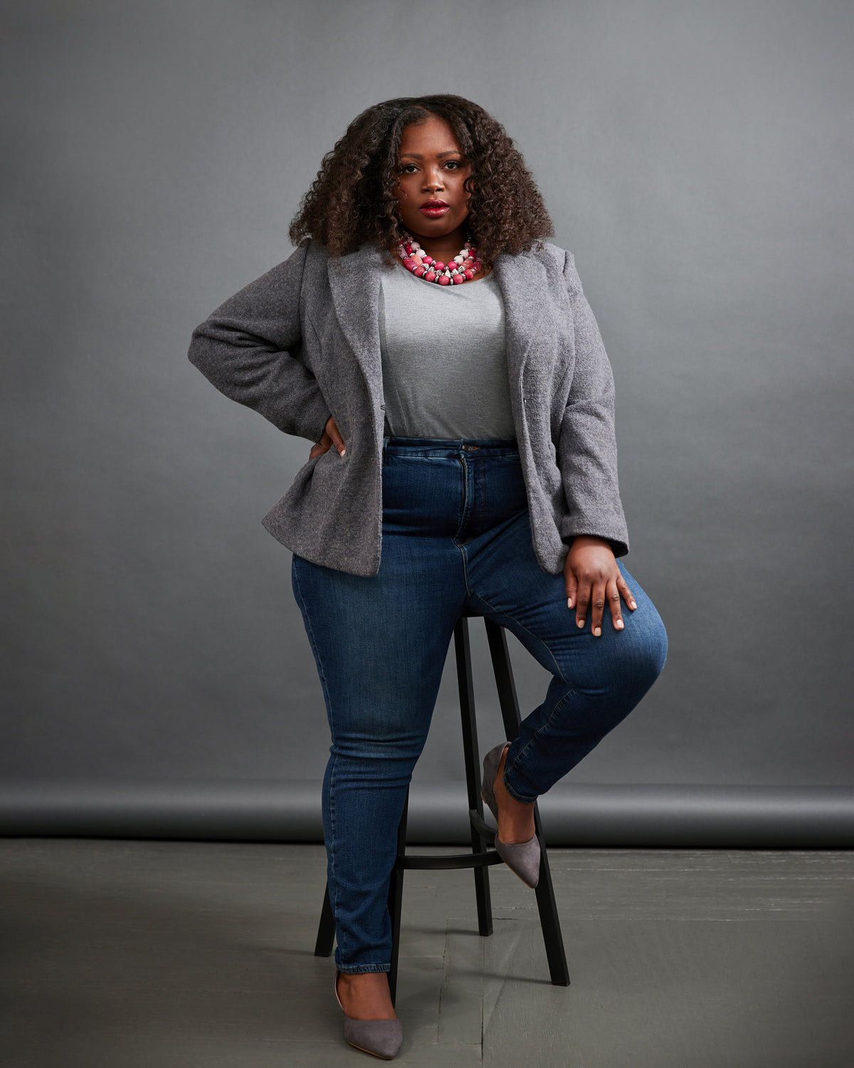 Cashmerette Auburn Blazer PDF sewing pattern, woman sitting on a stool wearing a gray cardigan, white shirt, blue jeans, and gray shoes