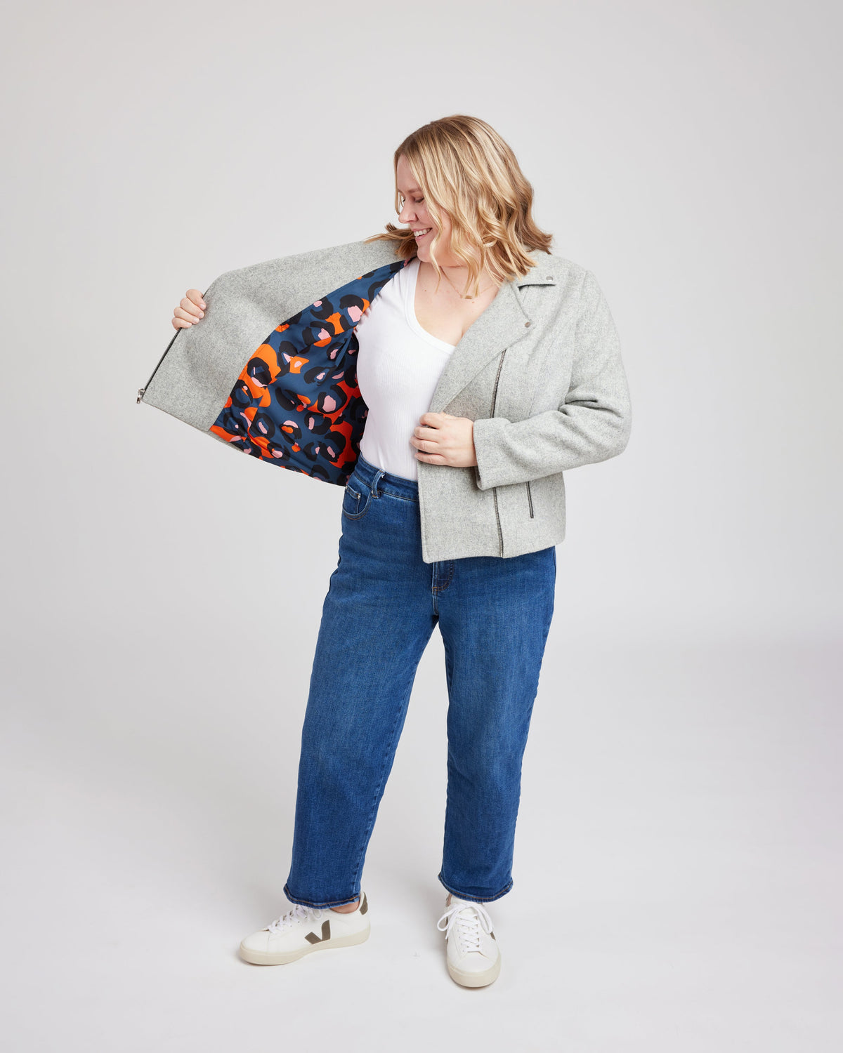 Cashmerette Canton Moto Jacket PDF sewing pattern, person wearing a gray jacket with a colorful lining, white shirt, blue jeans, and white sneakers