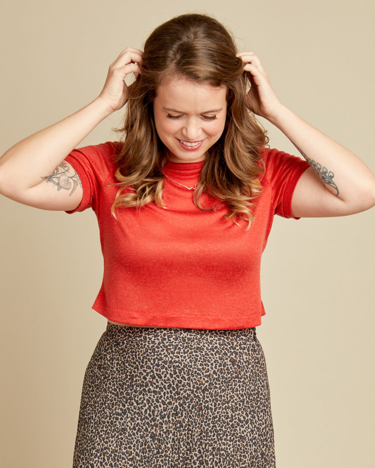 Cashmerette Concord T-Shirt PDF sewing pattern, woman wearing a red shirt and patterned skirt adjusting her hair
